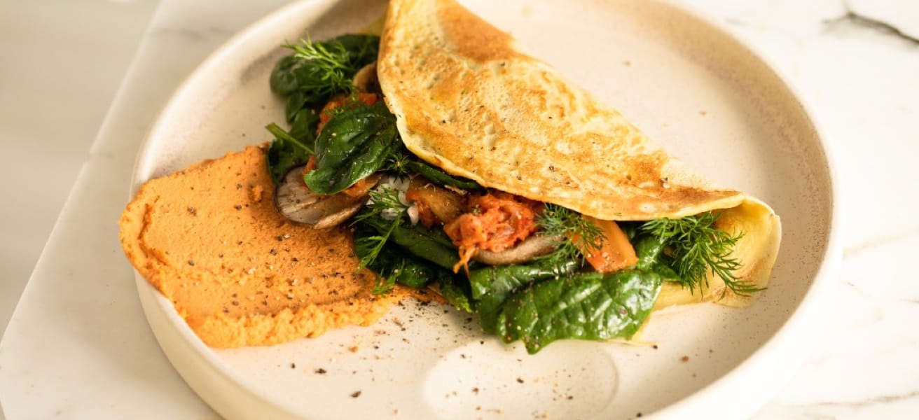 Golden-brown fluffy omelette garnished with herbs and spinach on a white plate.